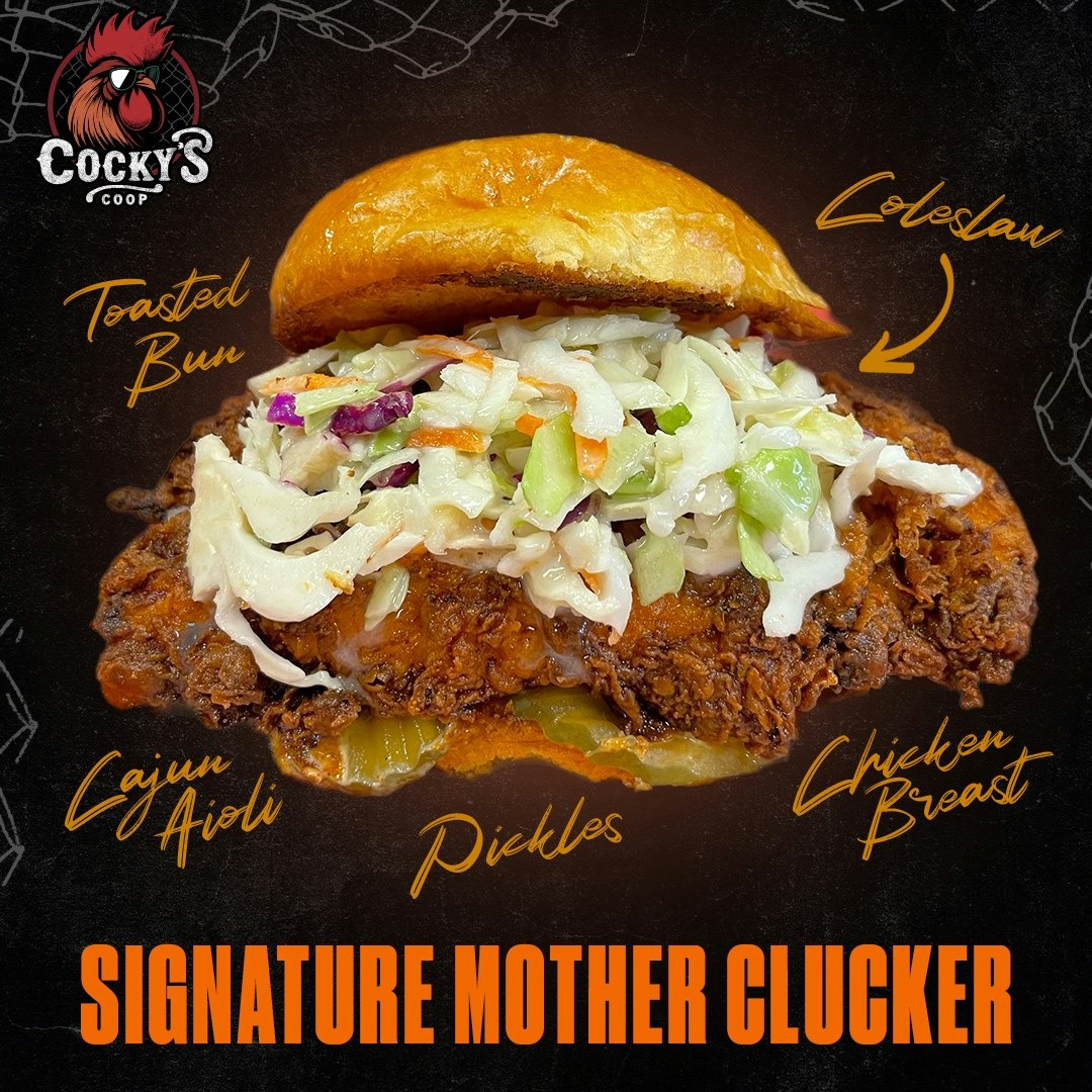 Signature Mother Clucker sandwich with a toasted bun, coleslaw, fried chicken breast, pickles, and Cajun aioli.