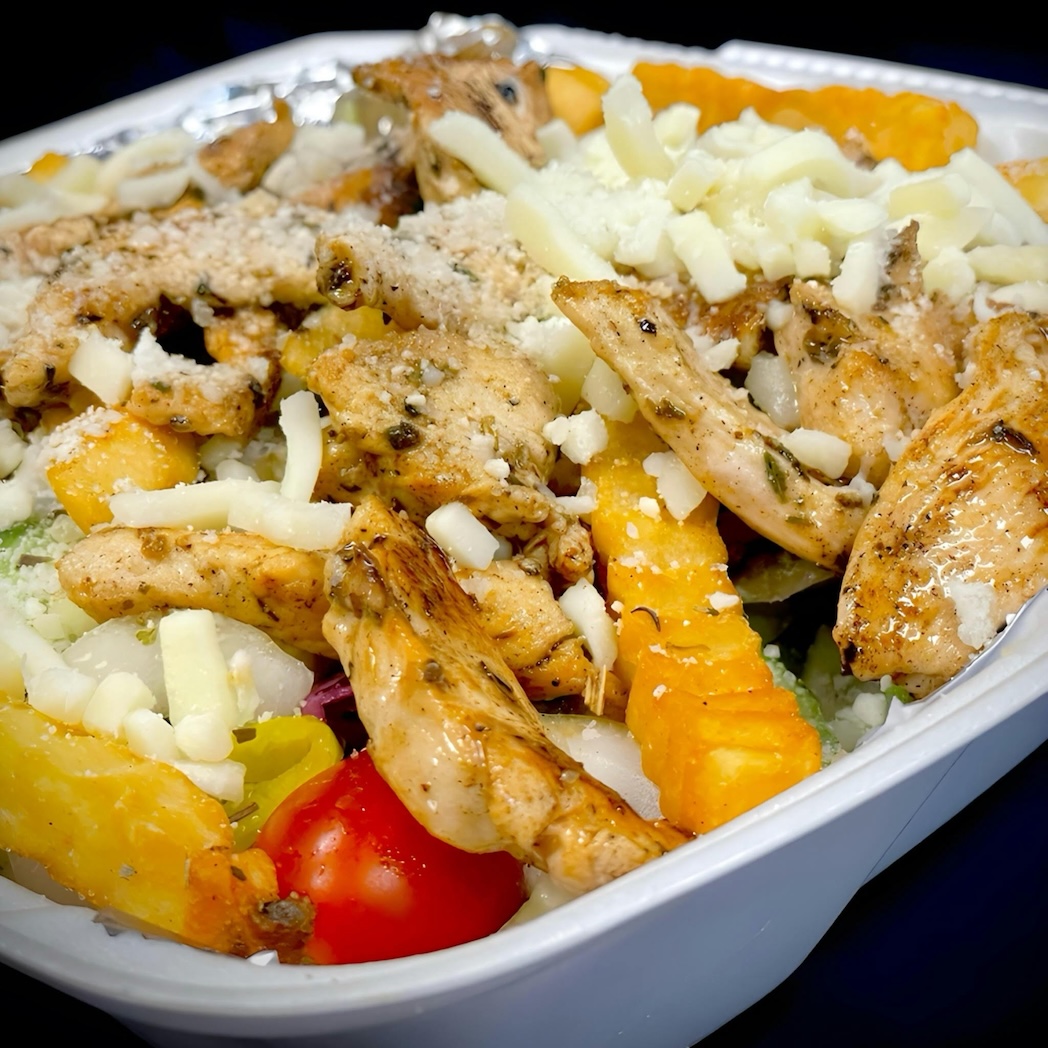 Takeout container with grilled chicken strips, crinkle-cut fries, shredded cheese, cherry tomato, and mixed vegetables.