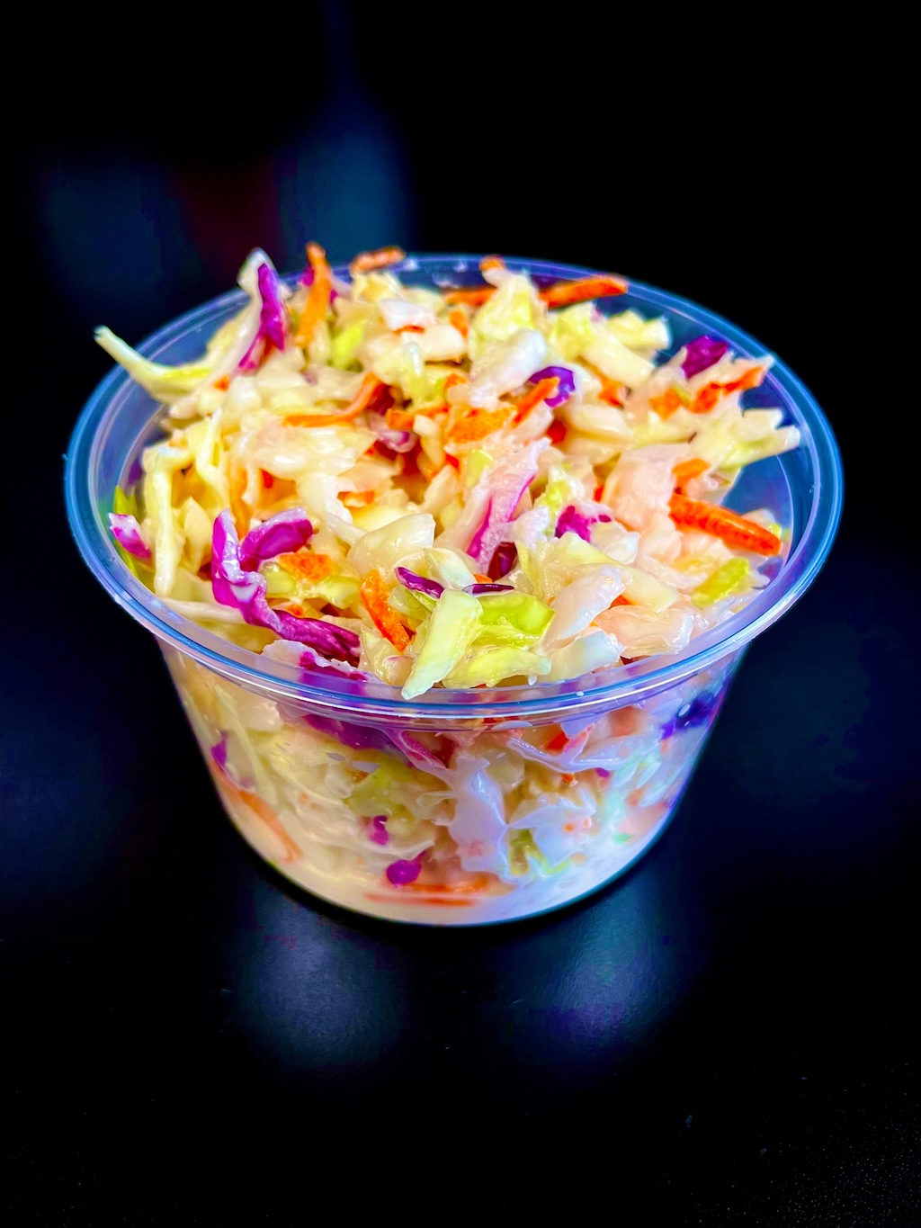 Clear plastic container filled with colorful coleslaw made of shredded cabbage and carrots in creamy dressing.