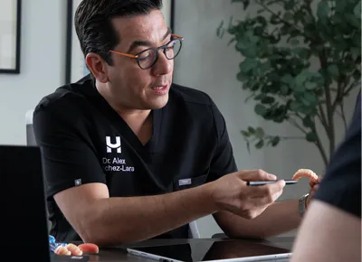 A man wearing glasses and black scrubs explains dental models while seated at a desk.