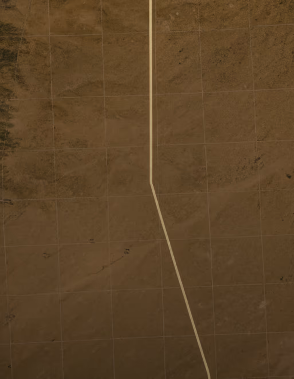 A straight dirt road running vertically in a barren, brown desert landscape with grid lines overlaid.