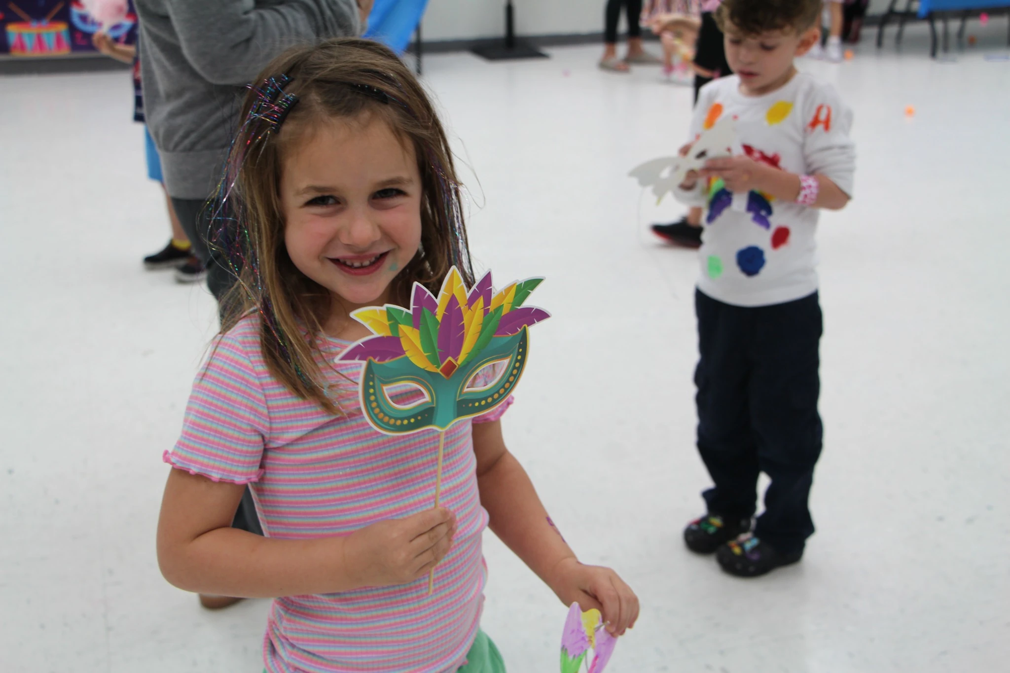 Smiling preschool child holding a colorful mask during a JCC aftercare arts and crafts activity