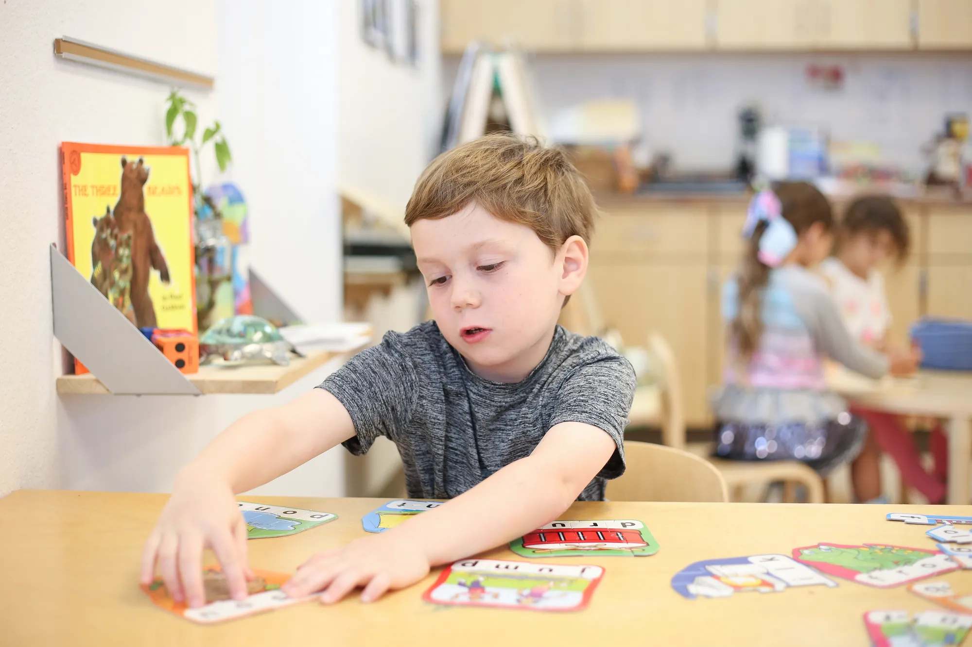 Preschool boy focused on completing a letter and word puzzle at a classroom table