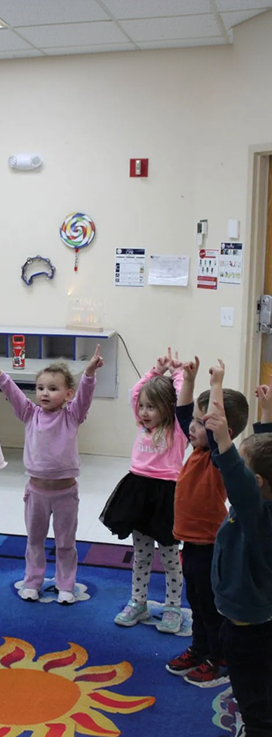 teacher and preschoolers raise arms in hands on learning at preschool boynton beach fl