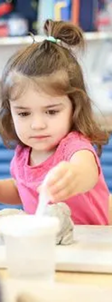 two year old girl in early childhood education program works on fine motor skills with clay and hands on activities