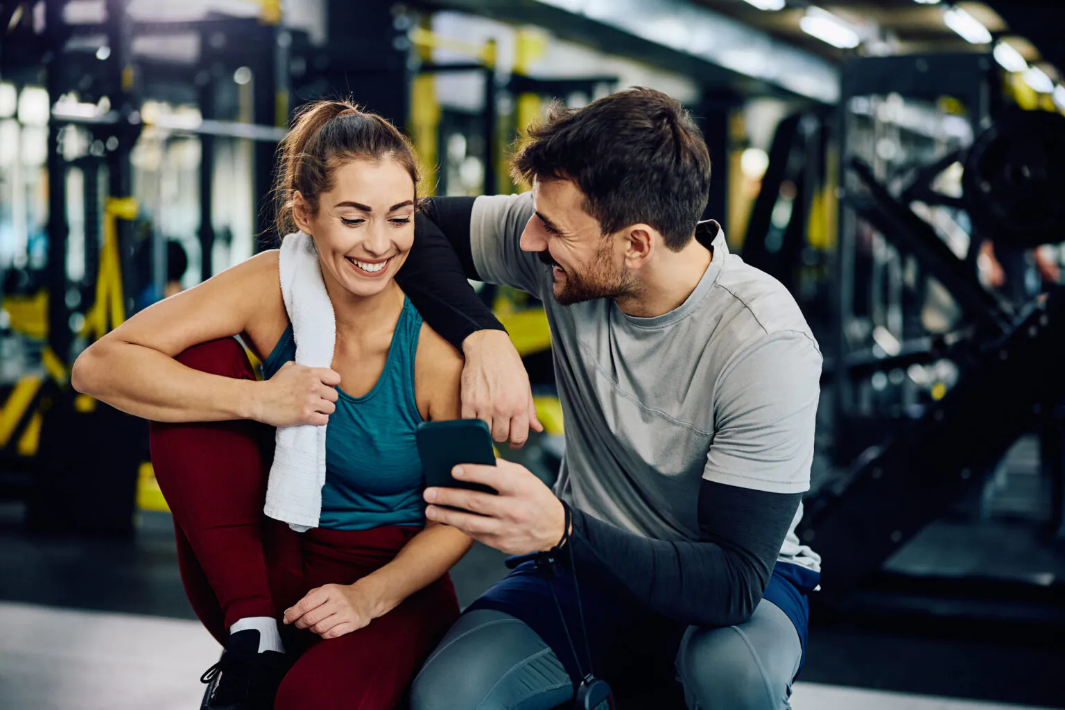 Two people at a gym smiling while looking at a phone together, using Nina, NCH's 24/7 digital care guide.