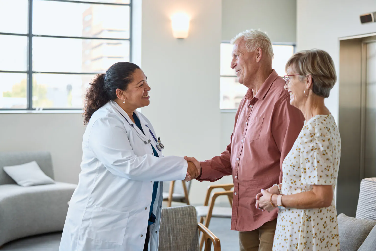 Doctor greeting an older couple with a handshake in a clinic, representing care navigation with Nina at NCH."