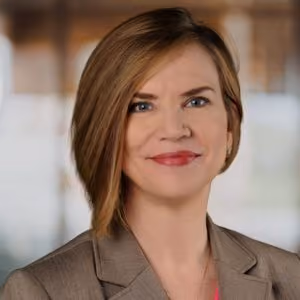 Professional headshot of a woman with short brown hair wearing a brown blazer smiling.