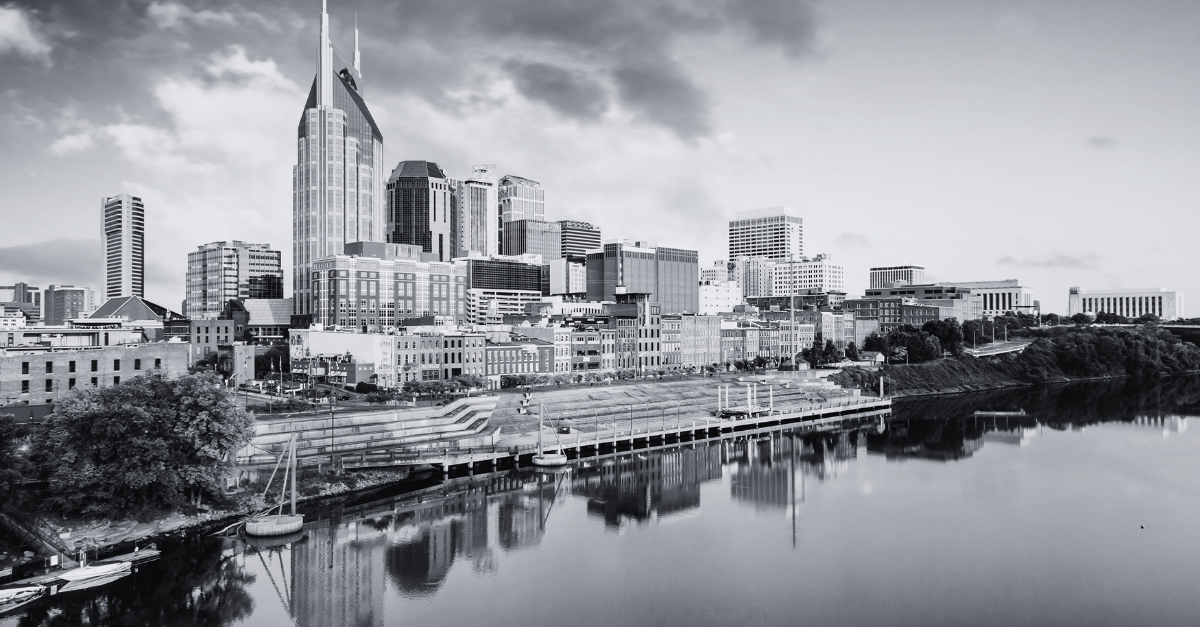 Black and white cityscape of Nashville skyline with skyscrapers and buildings reflected in calm river water.