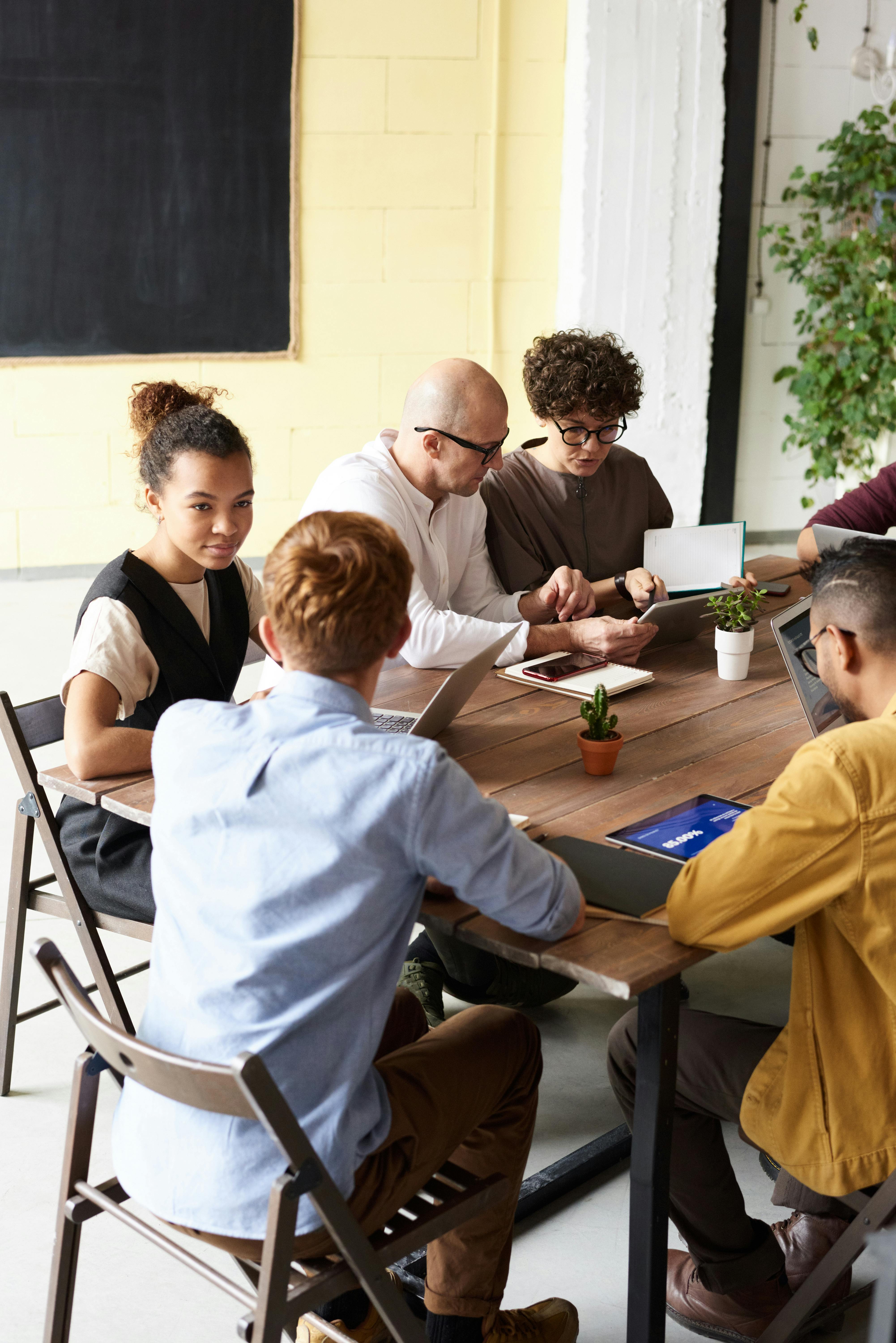 A diverse group of five people collaborating around a table with laptops and notebooks.