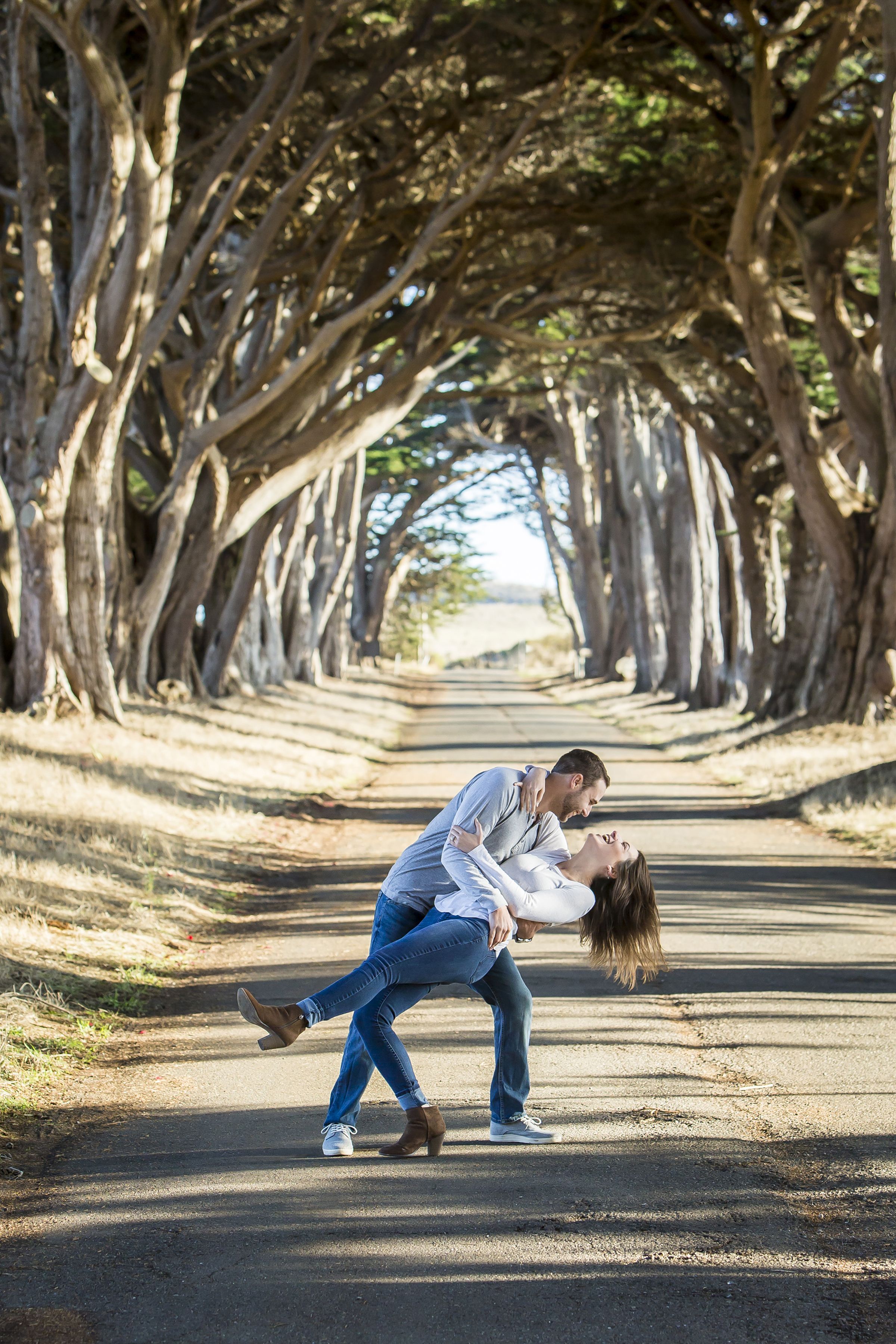 A couple embraces on a county road with trees lining both sides