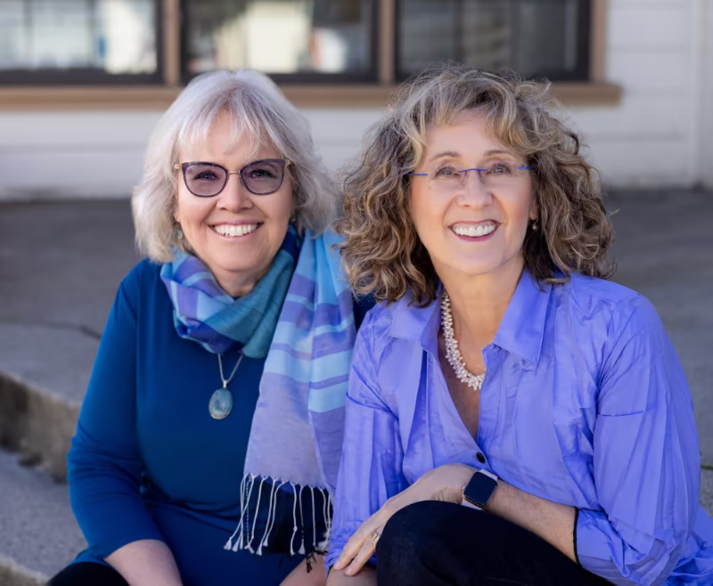 Erin Hutchins and a colleague smiling, seated outdoors in blue