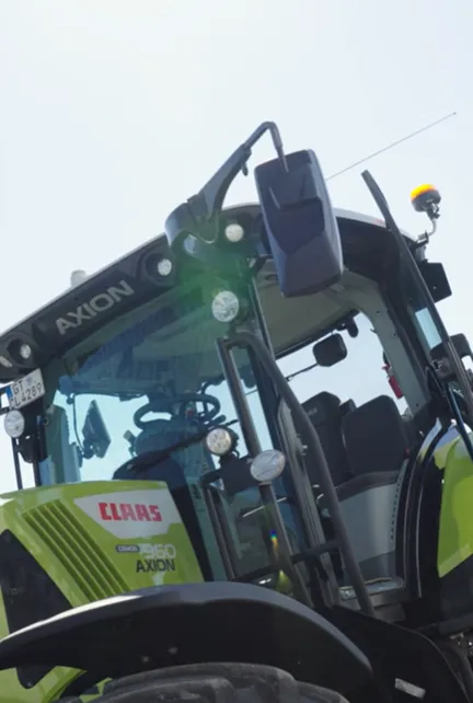 Nahaufnahme eines grünen Claas Axion 950 Traktors mit sichtbarer Fahrerkabine und Außenspiegel.