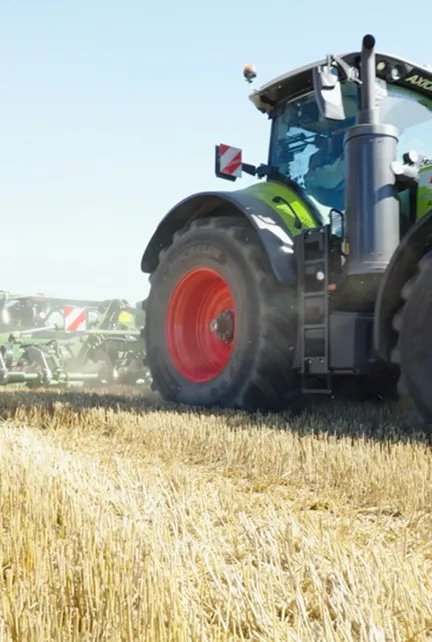 Ein Traktor mit roten Reifen fährt auf einem Feld mit abgeerntetem Getreide unter blauem Himmel.