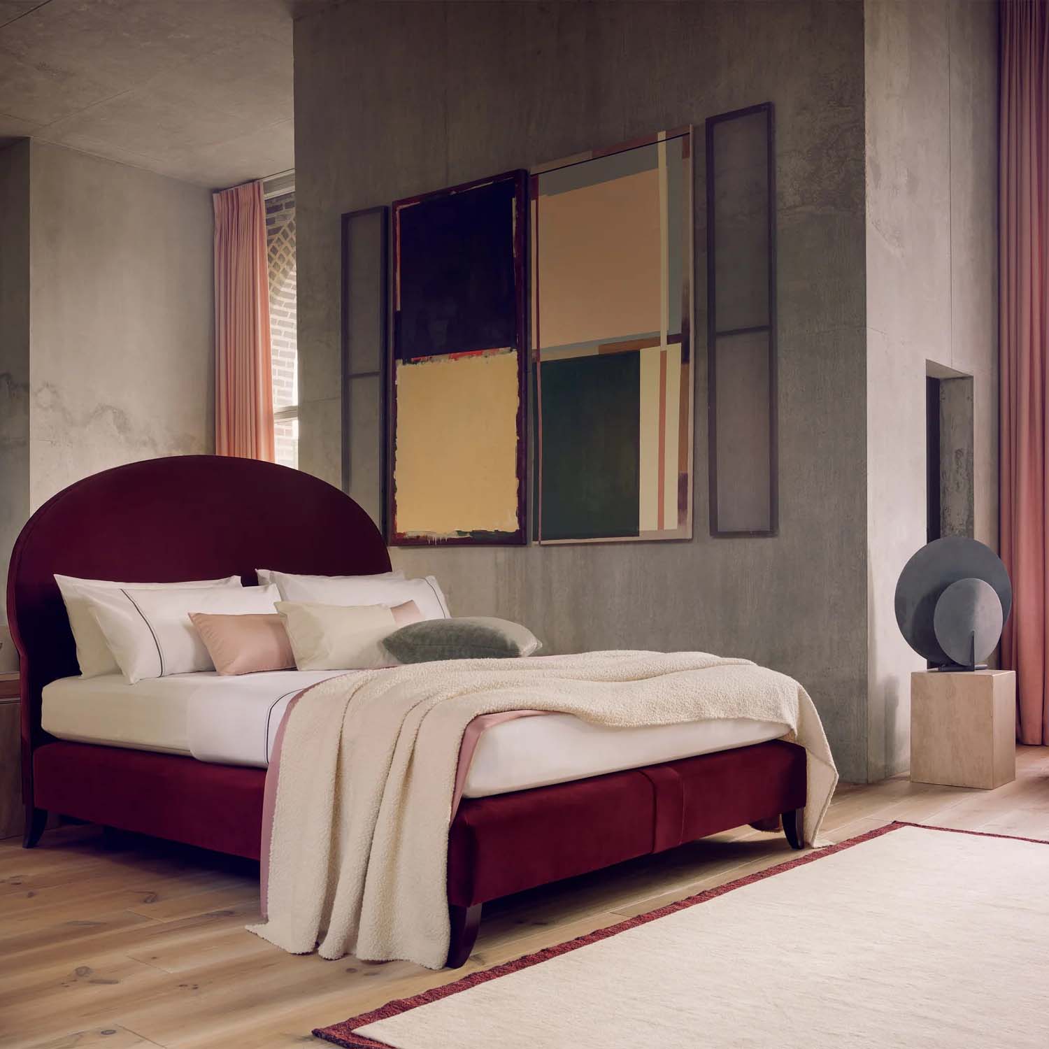 Modern bedroom with Savoir bed set. Burgundy upholstered rounded headboard bed, light bedding, abstract wall art, and wooden floor.