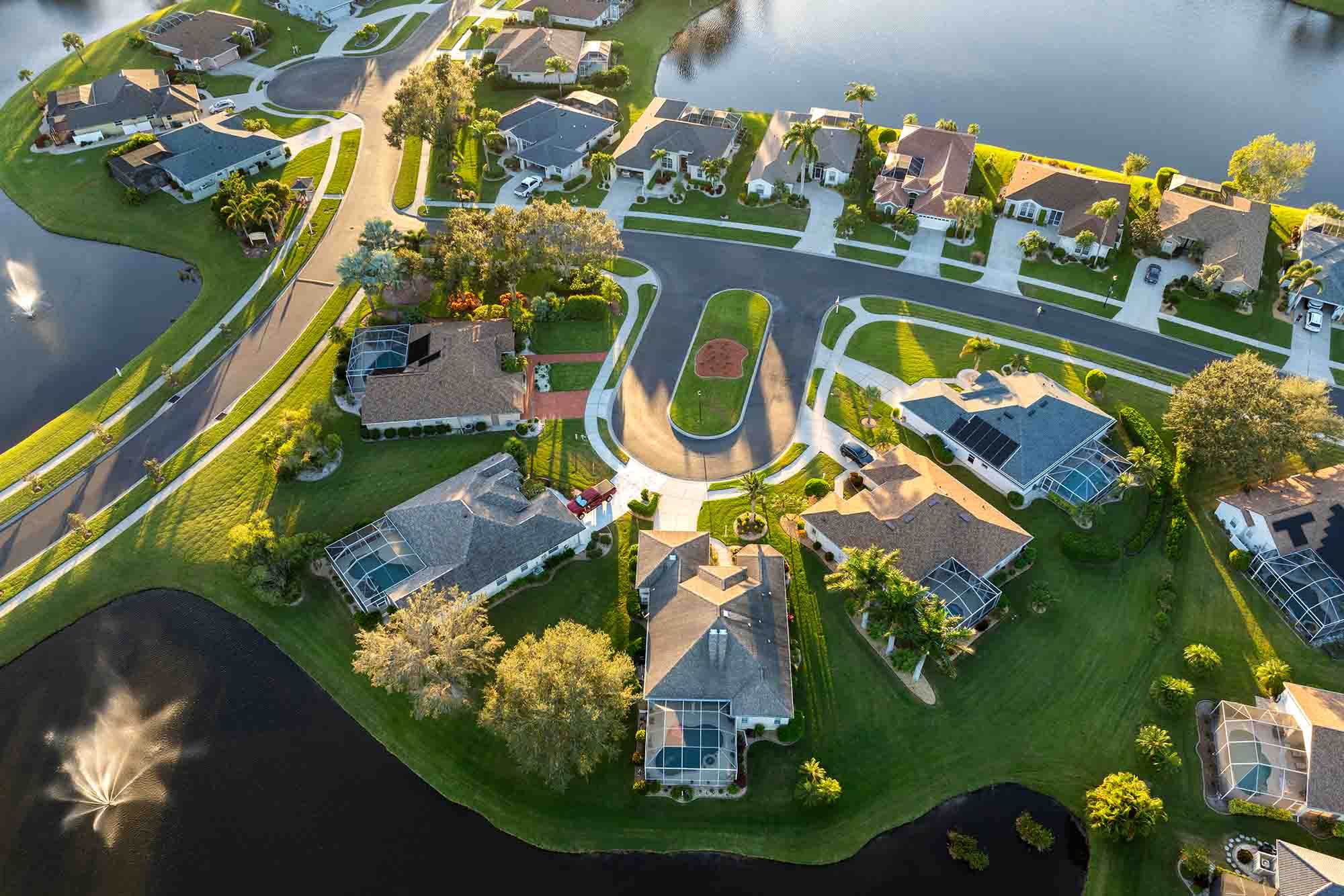 Aerial view of a suburban neighborhood featuring single-family homes with lawns, screened pools, and water fountains in nearby ponds.