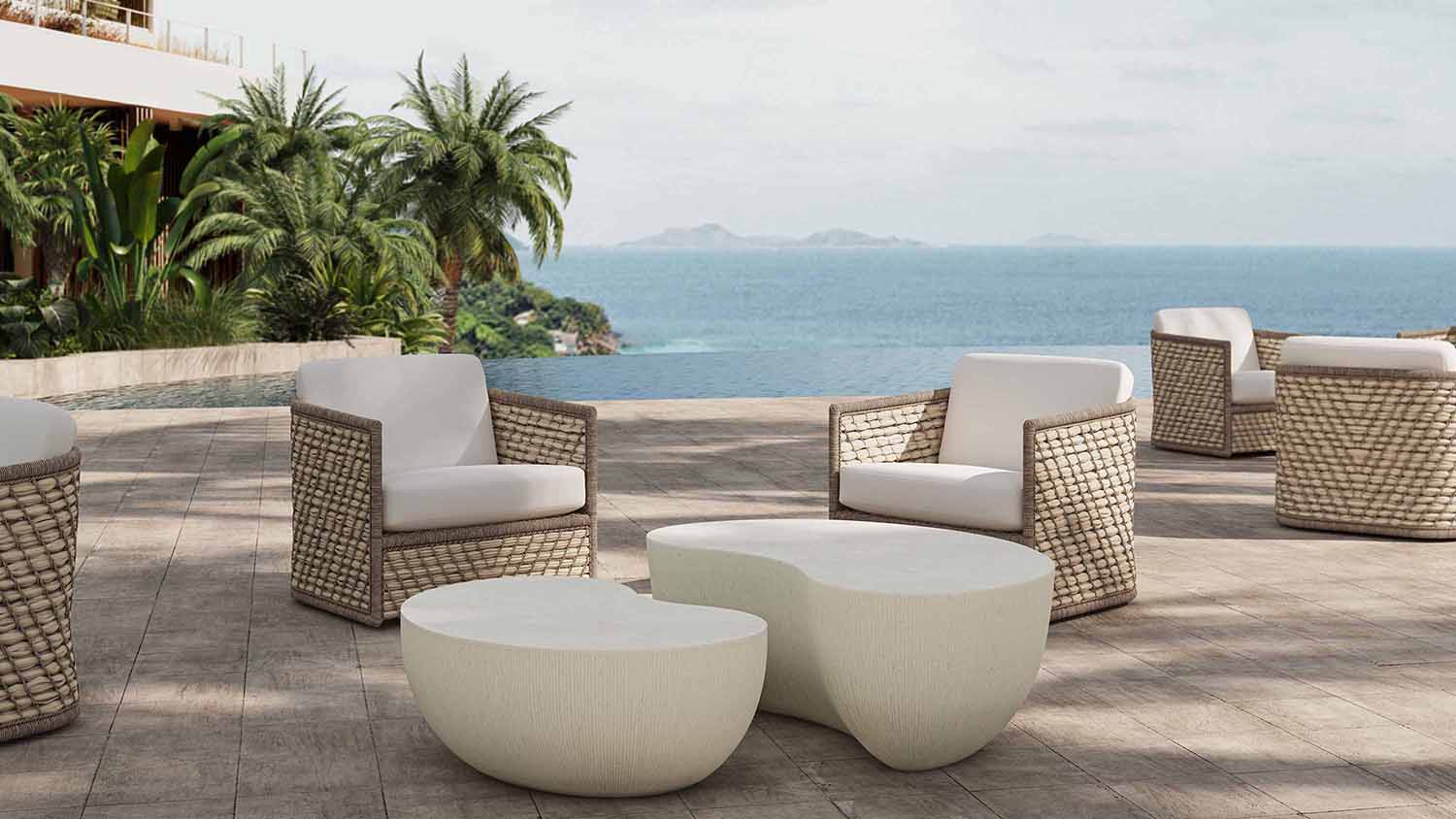 Outdoor patio with wicker armchairs and two abstract white tables overlooking an infinity pool and ocean.