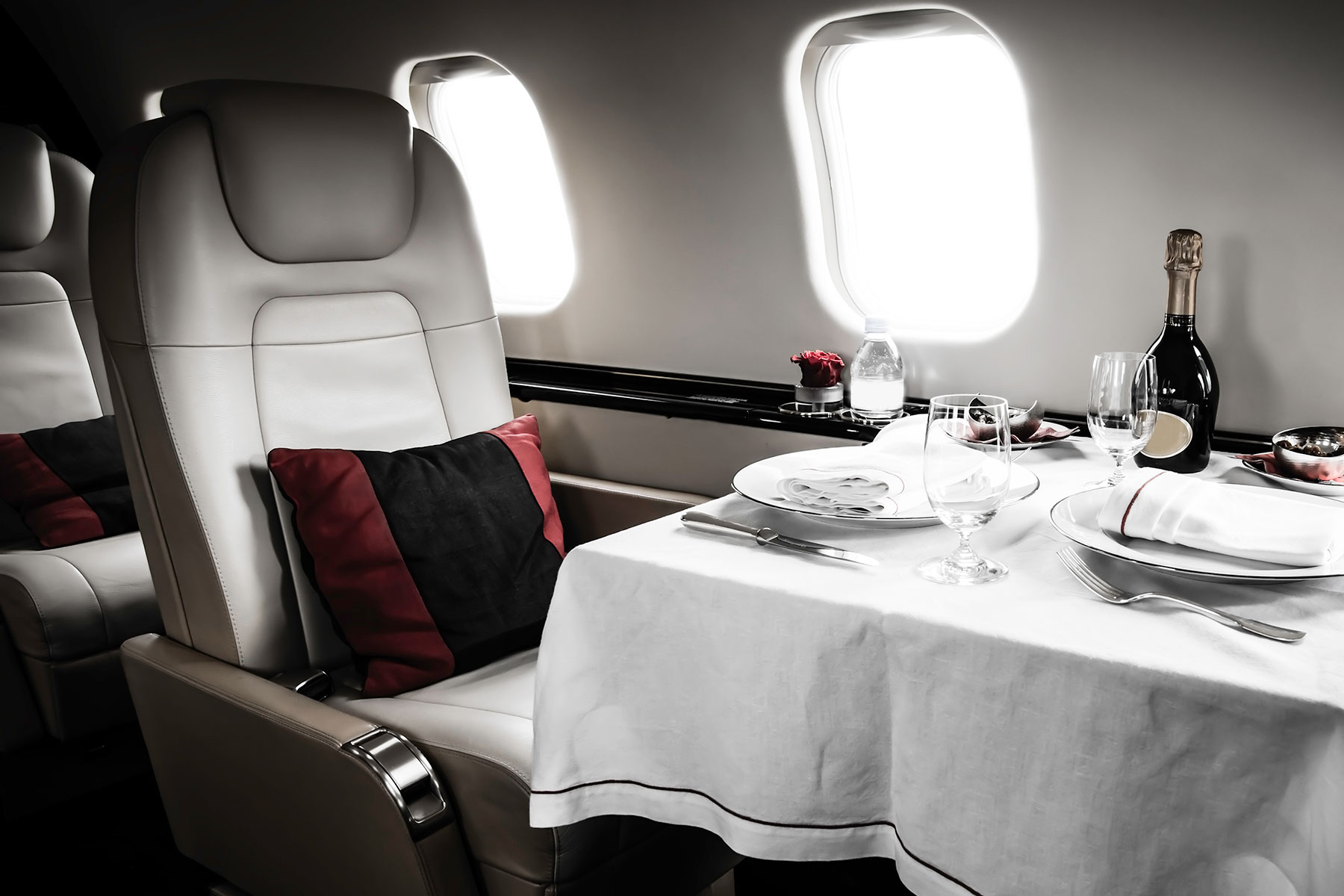Luxurious private jet bedroom with a large bed, two pillows, leather chair, and dark wood finish.