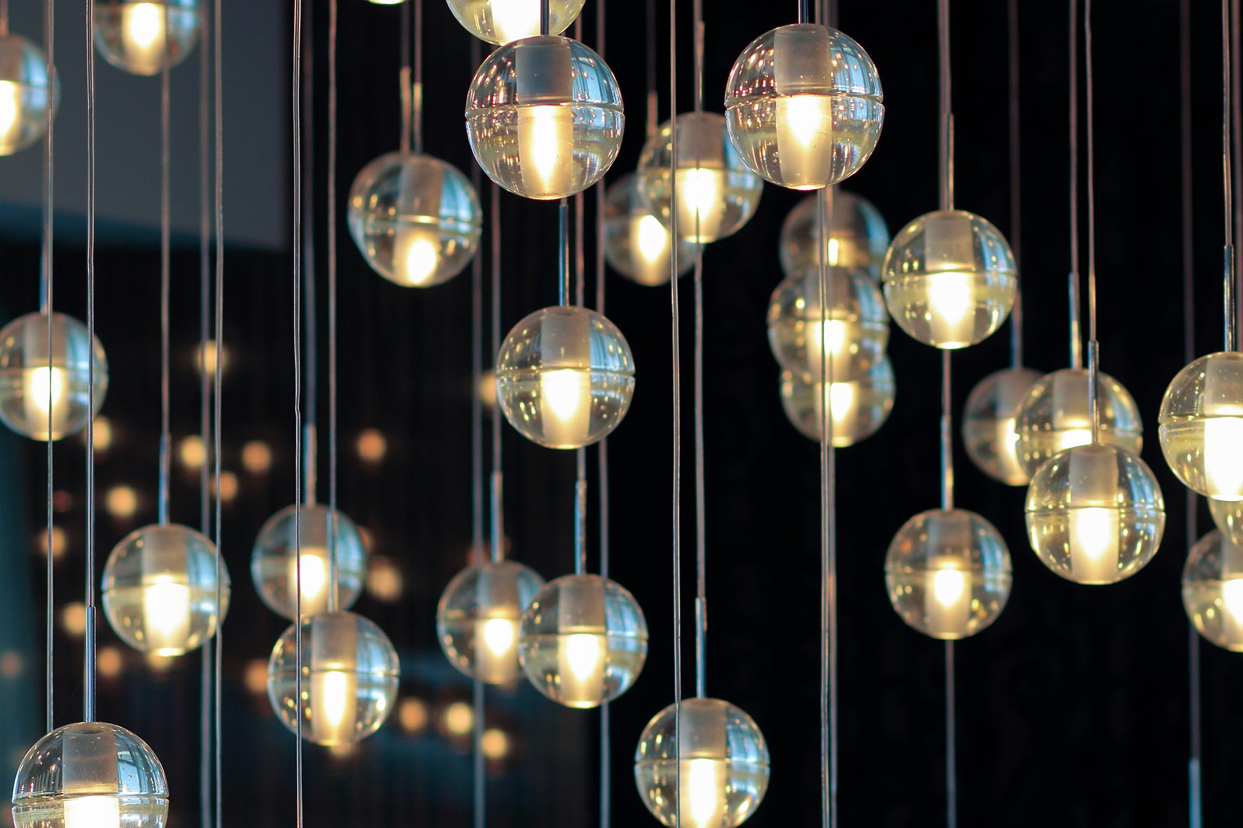 Modern chandelier with multiple glowing spherical glass pendants hanging at different heights.