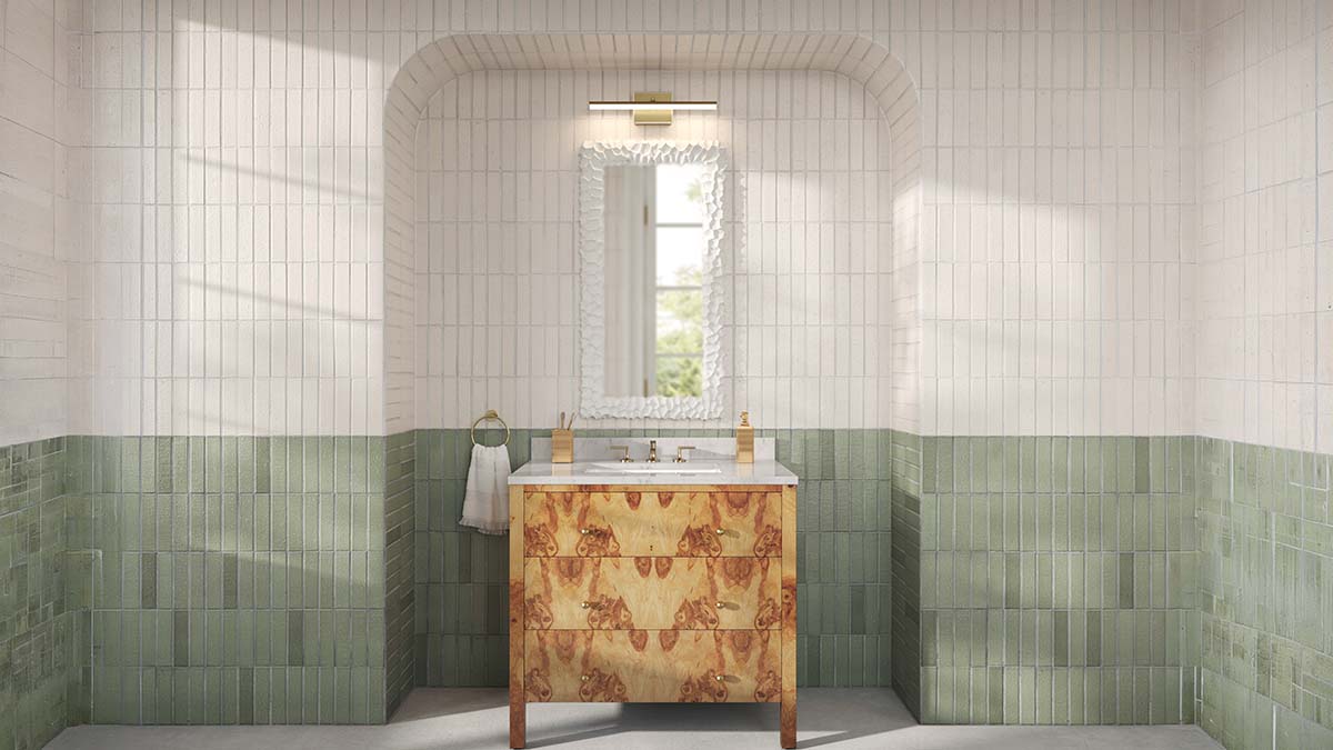 Bathroom vanity with marble countertop and wooden drawers beneath a decorative white framed mirror on a wall with green and white tiles.