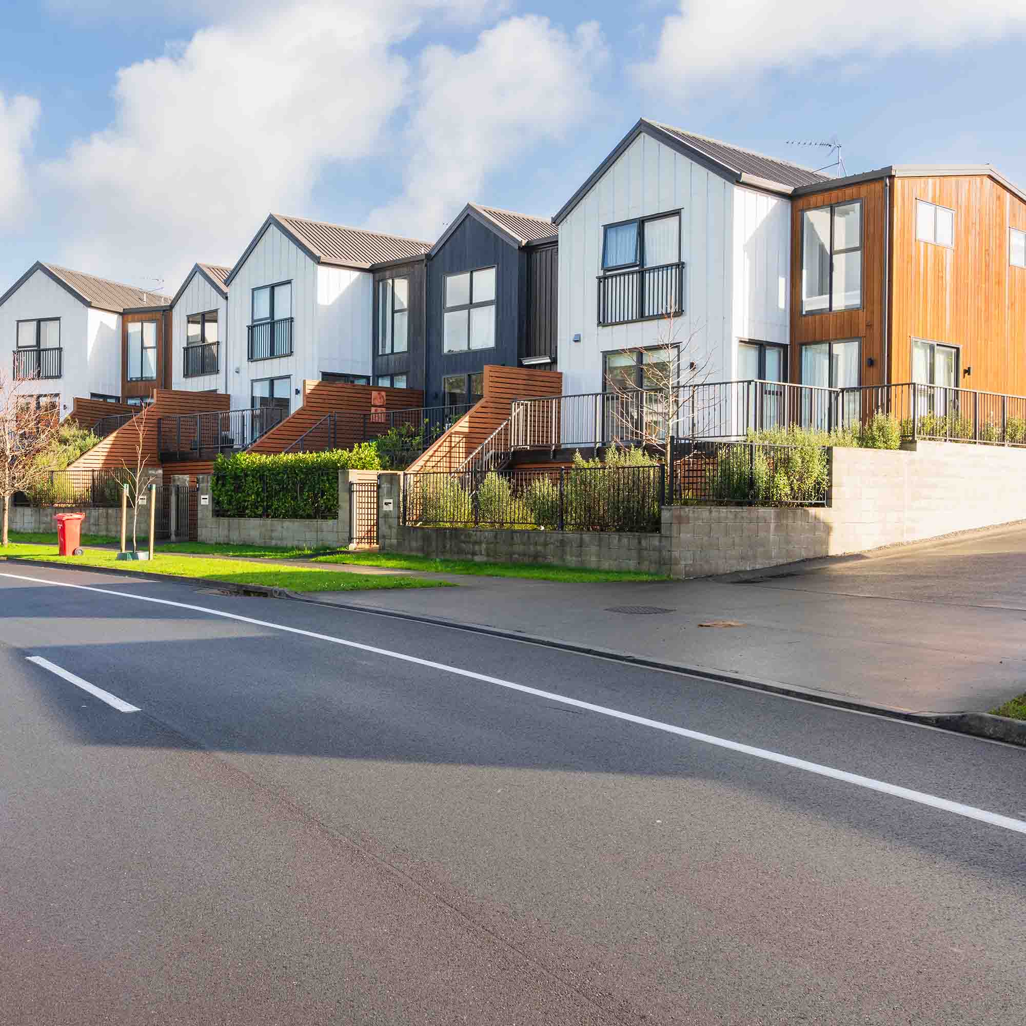 Row of modern townhouses with white, gray, and wooden exterior panels under a partly cloudy sky.