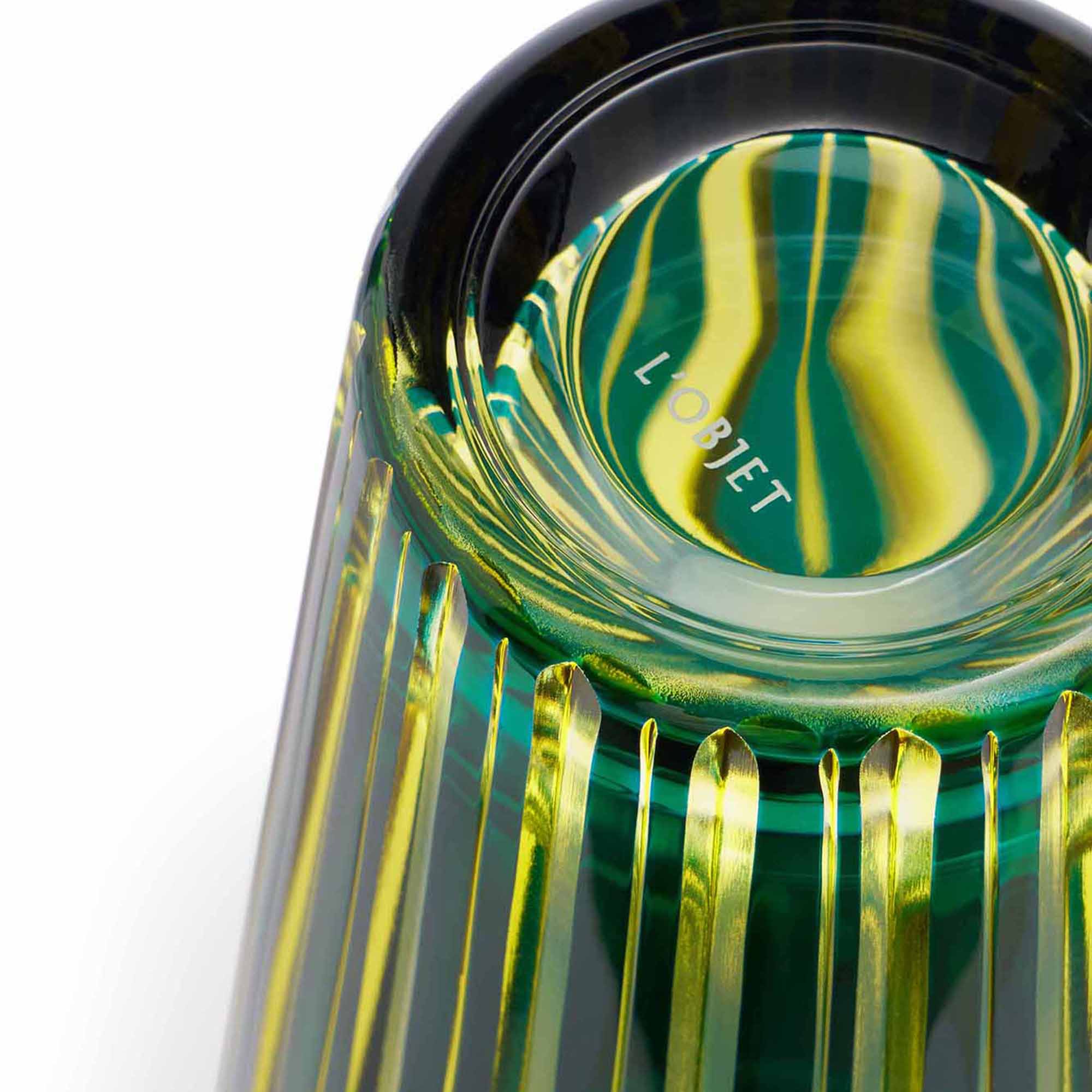 Close-up of a green glass object with vertical gold stripes and 'L'OBJET' engraved on the bottom.