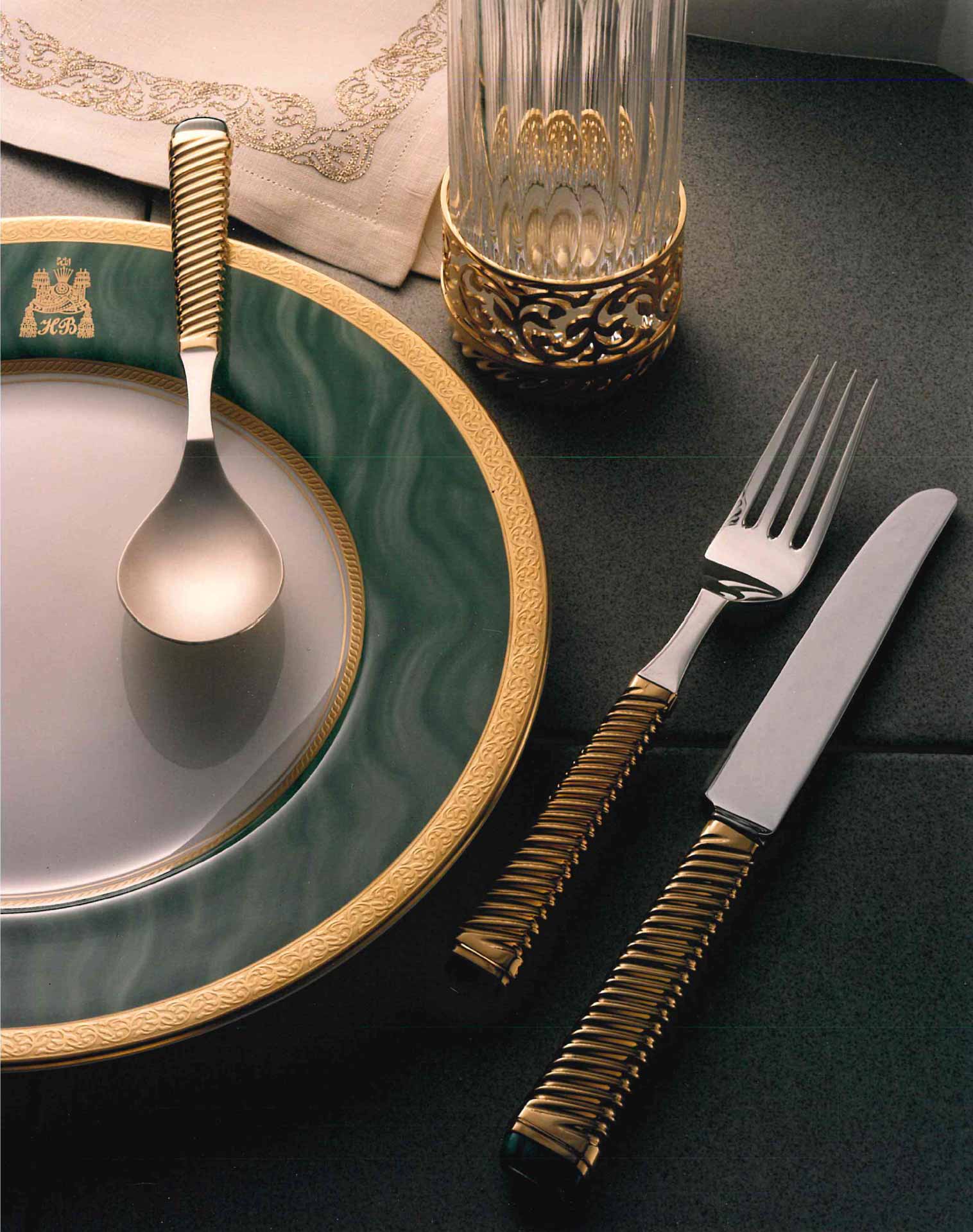 Elegant table setting with a green and gold-rimmed plate and gold-handled fork, knife, and spoon.
