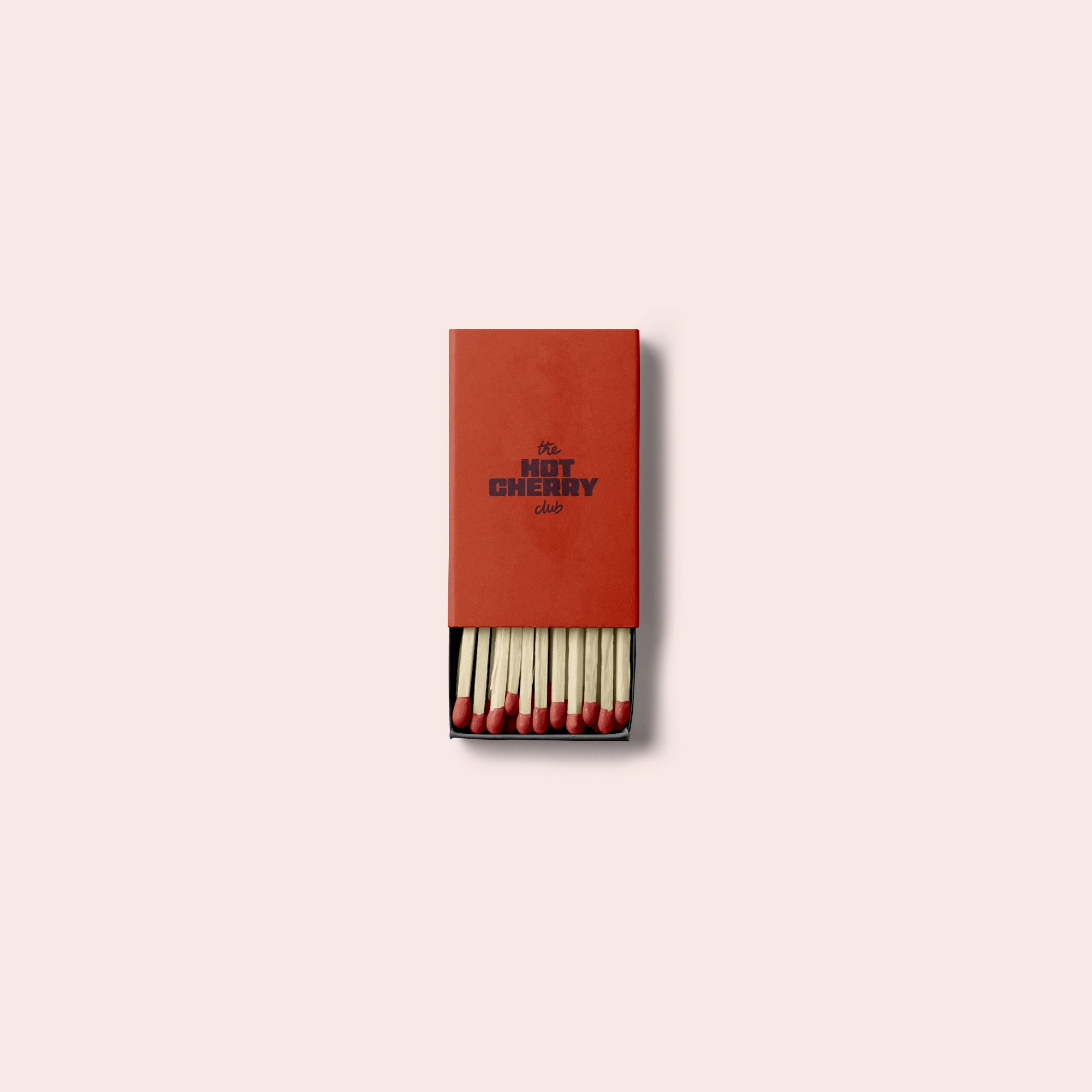 Open matchbox with red-tipped matches and red cover reading 'the HOT CHERRY club' on pale pink background.