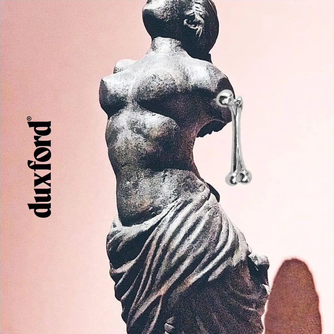 Ancient-style statue of a woman missing arms, with a modern metal bone replacing one arm, against a pink background with the word 'duxford' vertically on the left.