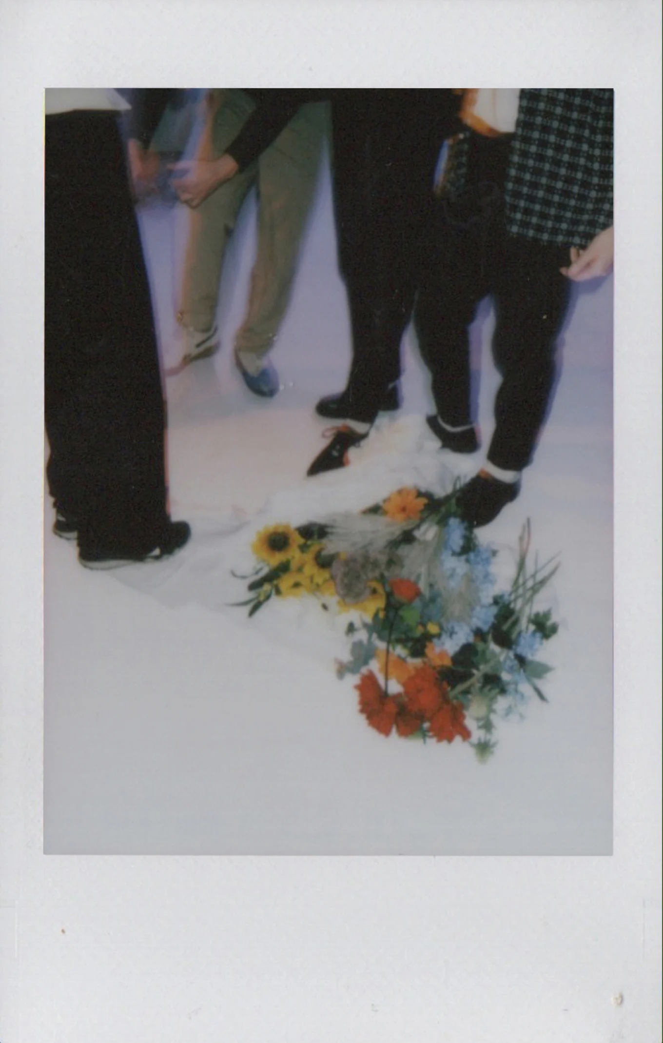 Group of people standing on a white surface with scattered bouquets of colorful flowers near their feet.