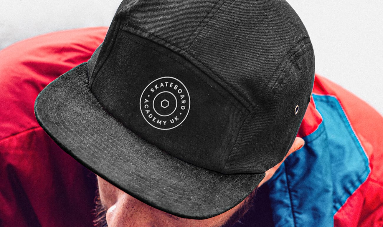 Person wearing a black cap with the logo text 'Skateboard Academy UK' and a red and blue jacket.