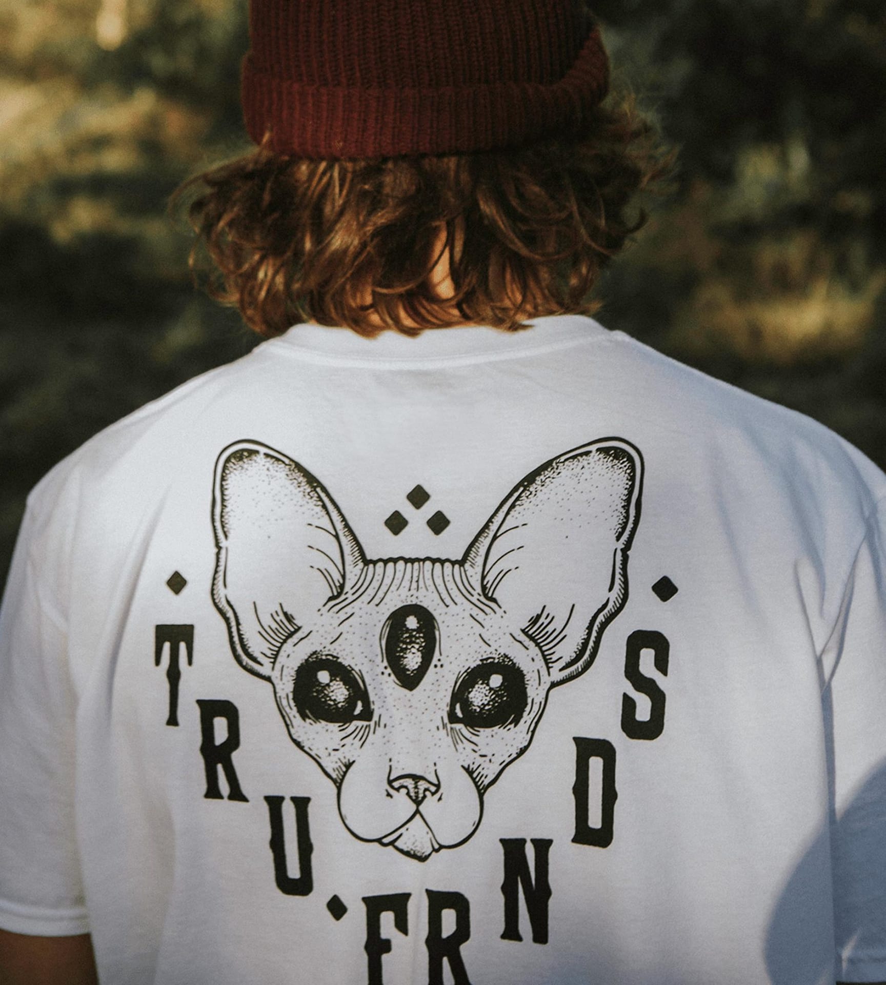 Person wearing white T-shirt with black graphic of a three-eyed cat face and the text 'TRU FRNDS' around it.