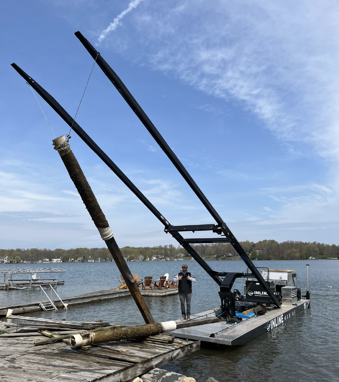 Inline Marine custom fork barge lifting a large log near a lakefront shoreline