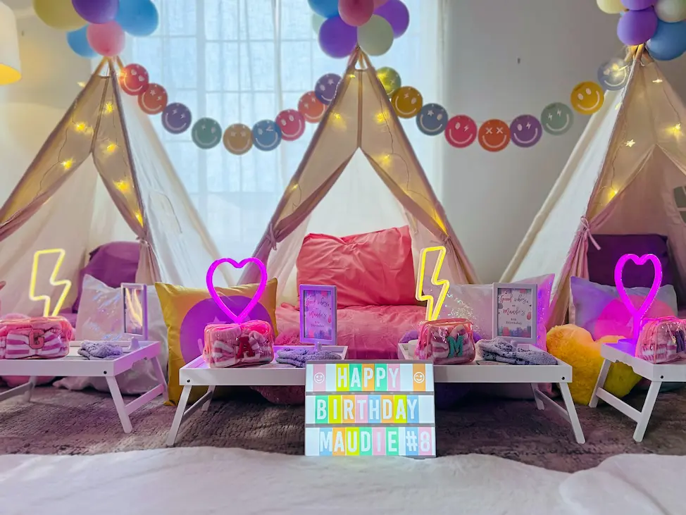 Indoor kids' birthday setup with teepees, balloons, lights, gifts, and a sign saying 'Happy Birthday Maudie #8'.