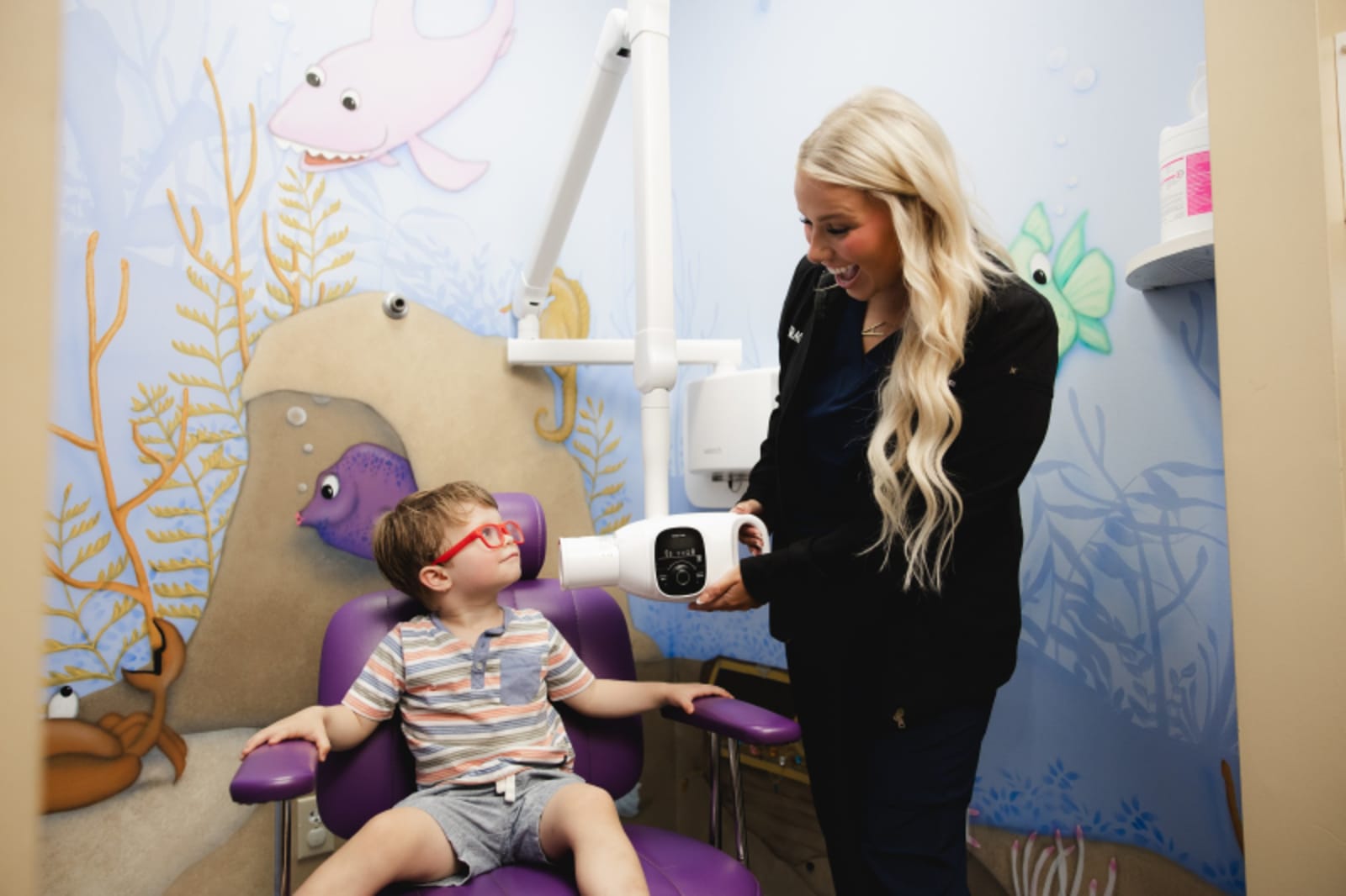 Dentist demonstrating oral evaluation technique to a young patient in treatment chair