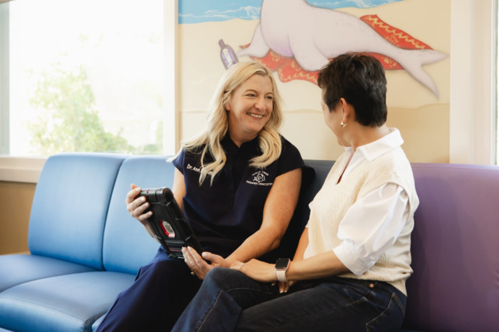 Dental hygienist explaining teeth model to parent and child in treatment room