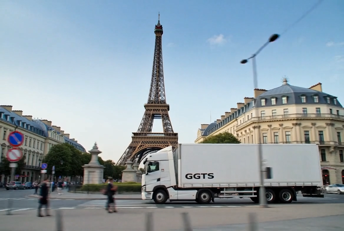 Camion blanc marqué GGTS en circulation près de la Tour Eiffel à Paris avec des bâtiments haussmanniens en arrière-plan.