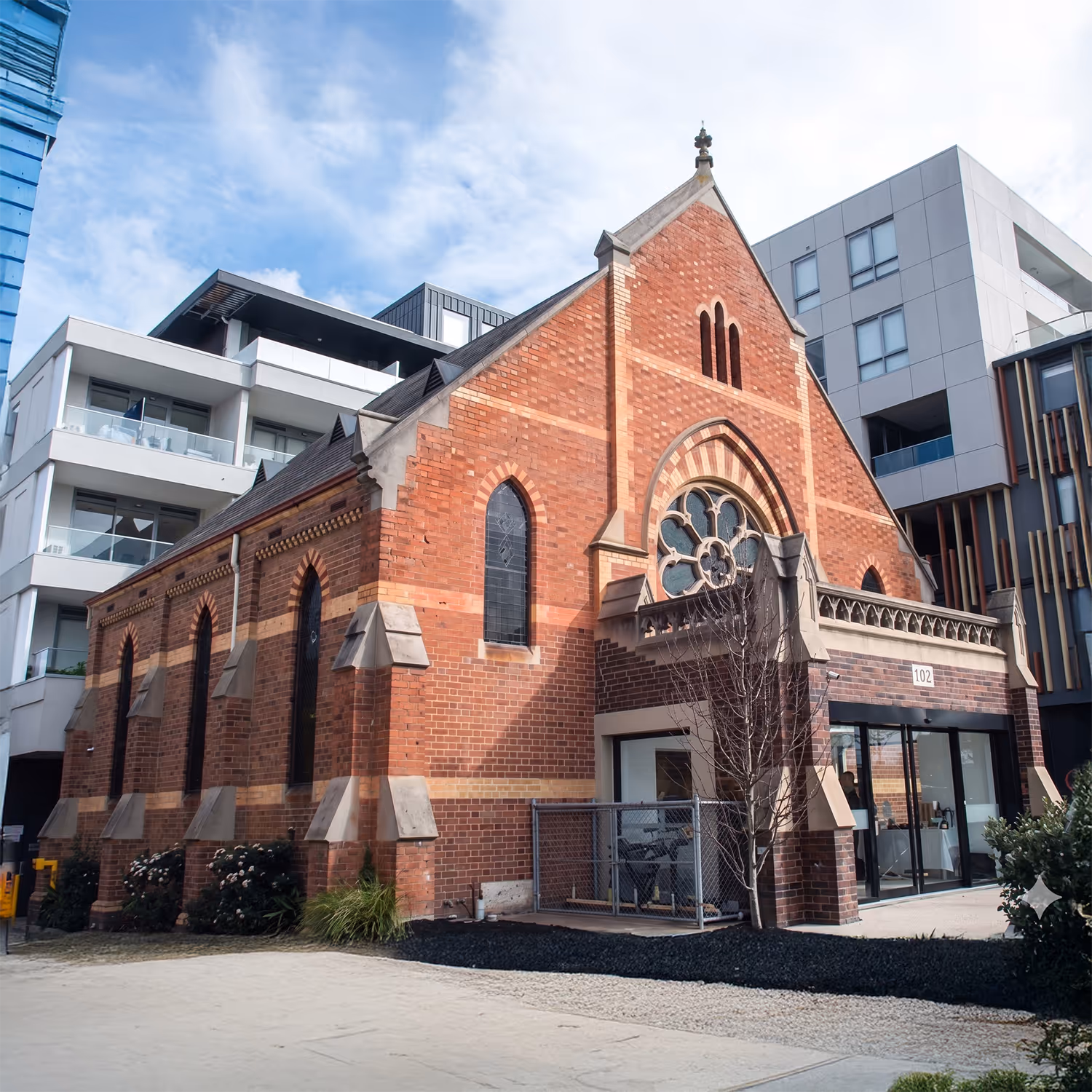 A heritage brick church building with gothic-style windows, converted into a modern clinic, set beside urban apartments.