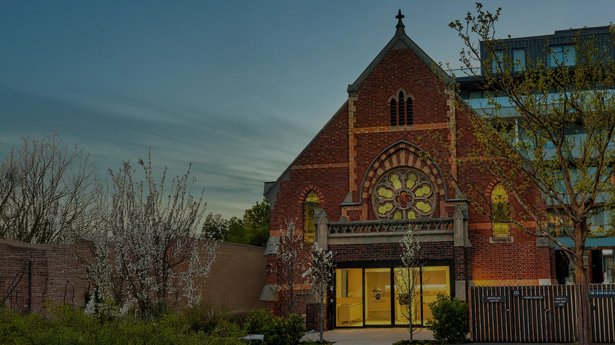 Historic brick church with stained glass windows and modern entrance at dusk.