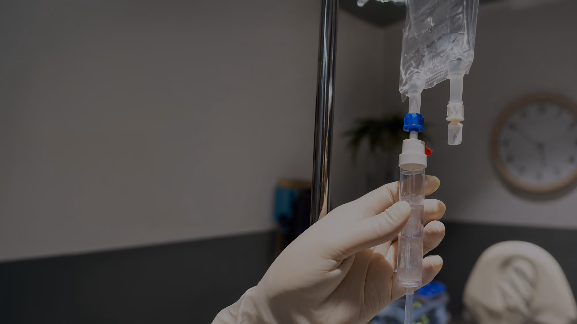 Gloved hand adjusting a drip chamber on an intravenous (IV) fluid bag in a medical setting.