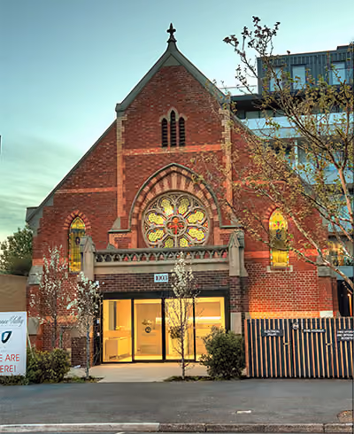 A heritage red brick church featuring a large rose window, repurposed into a modern clinic with a glass-fronted entrance.