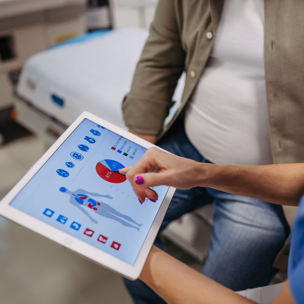 Healthcare professional explaining metabolic syndrome results to a patient using a tablet displaying body and health data in a clinical consultation room.