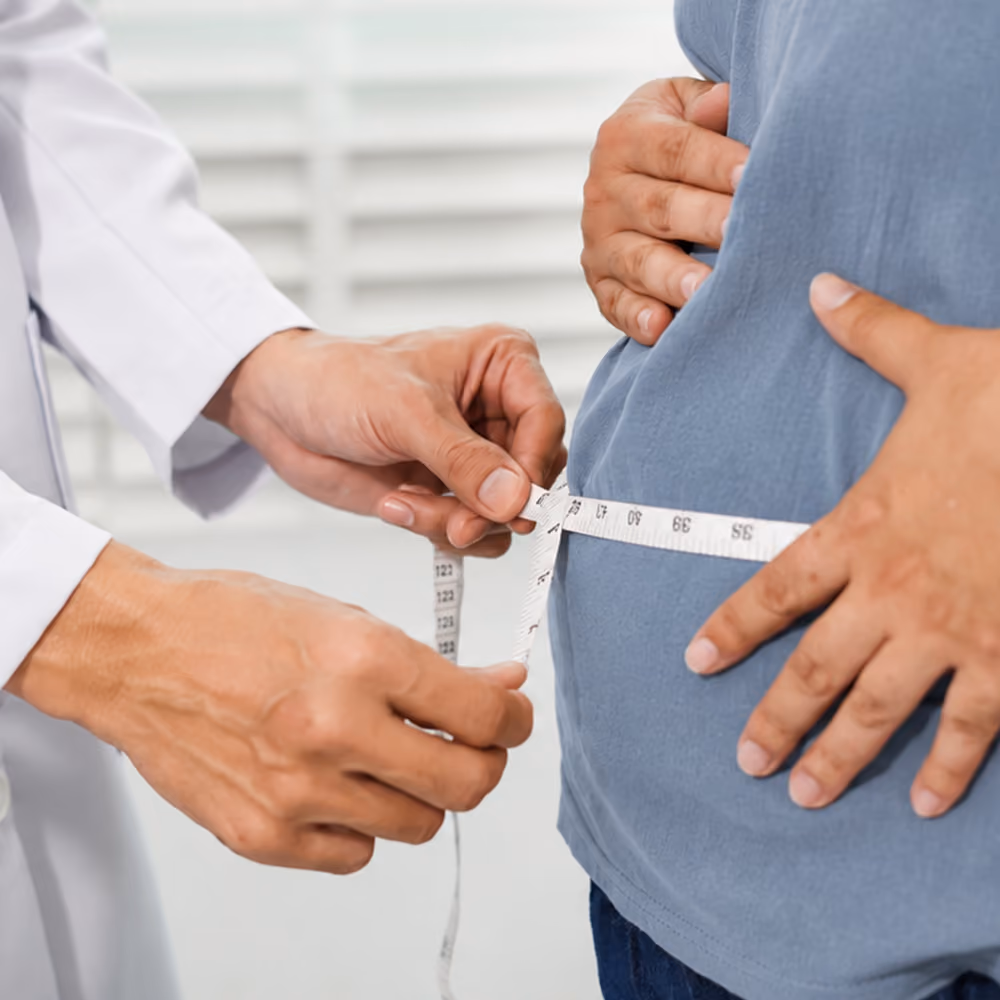 Healthcare professional measuring a patient's waist circumference with a tape measure during an assessment for metabolic syndrome or obesity in a clinical setting.