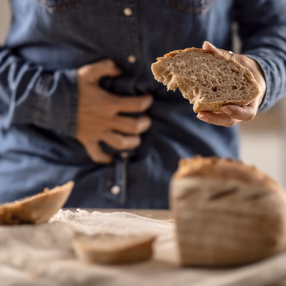 Person holding a slice of bread while experiencing abdominal discomfort, illustrating symptoms commonly associated with coeliac disease.