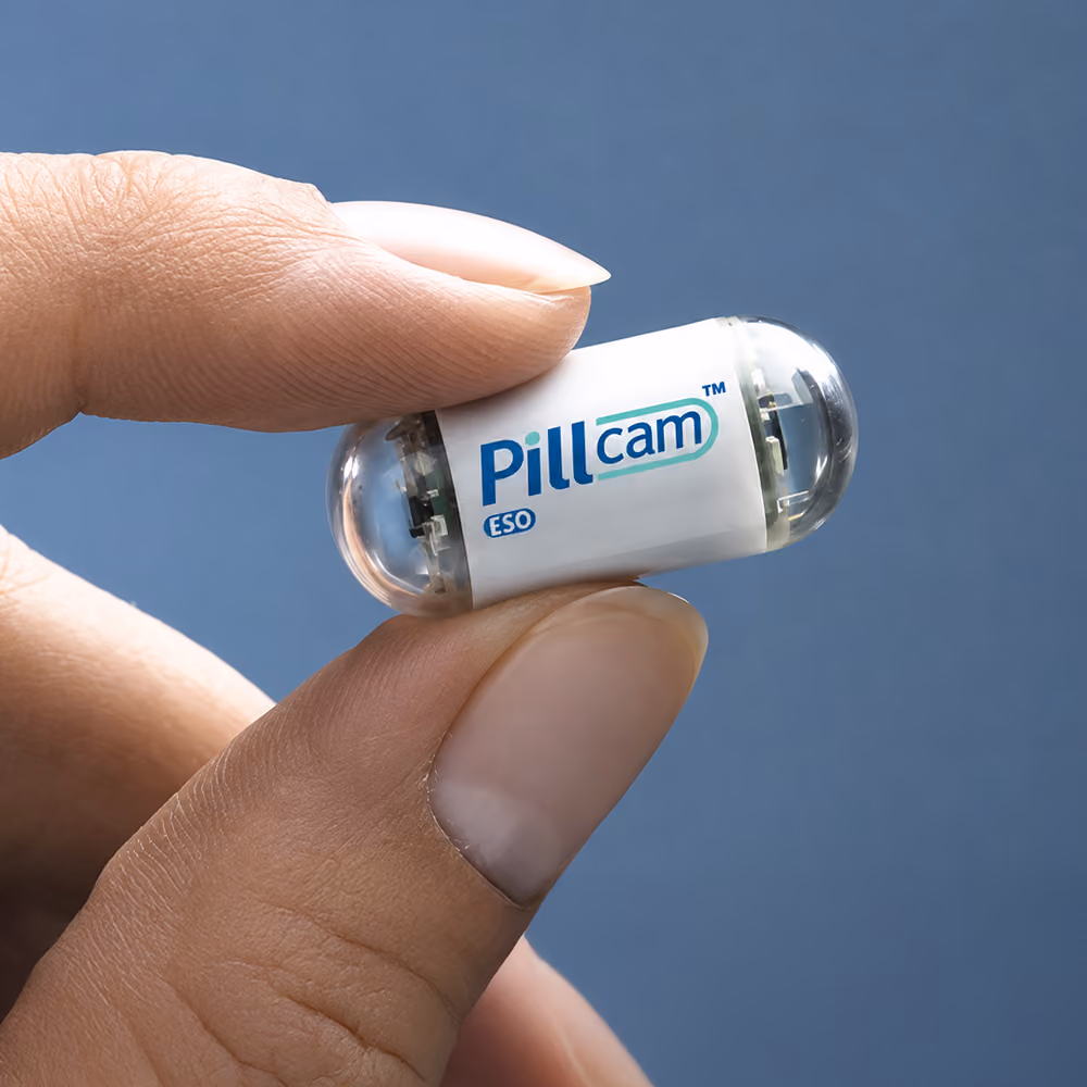 A PillCam SB 2 capsule endoscopy camera, used to non-invasively film the small intestine, sits on a wooden surface.