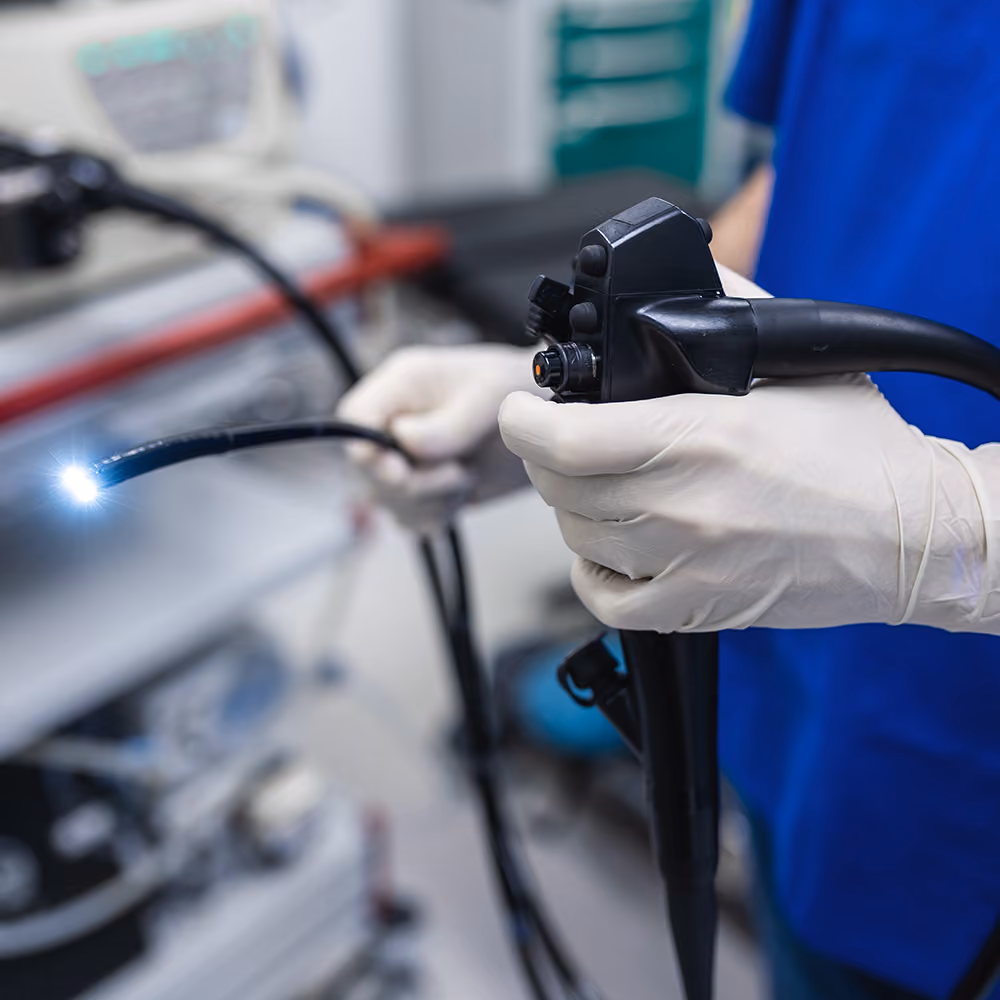 Gloved medical staff hold an endoscope while preparing a patient for a gastroscopy in a clinical hospital room.