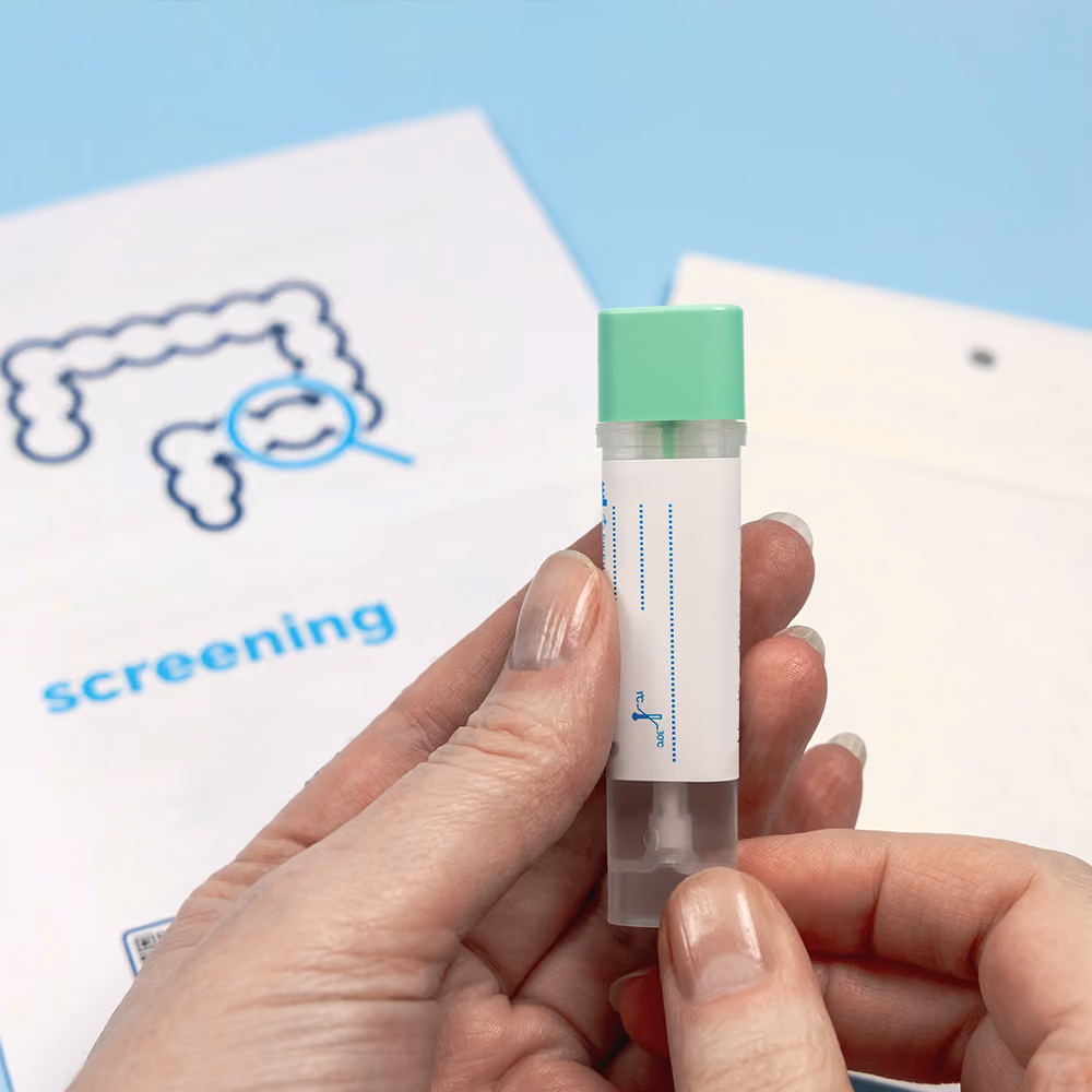 Person holding a bowel cancer screening test kit with a screening information booklet in the background.