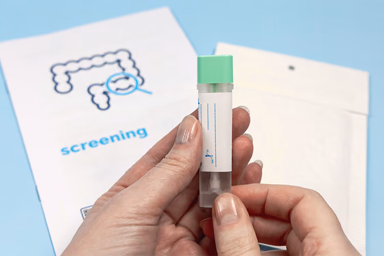 Person holding a bowel cancer screening test kit with a screening information booklet in the background.