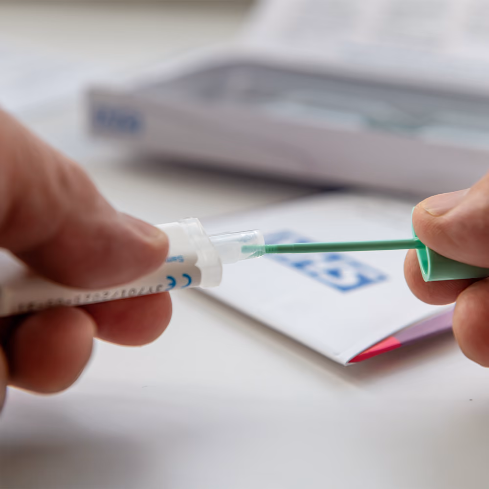 Close-up of a person preparing a bowel cancer screening test kit by inserting the sample collection probe into the specimen tube.