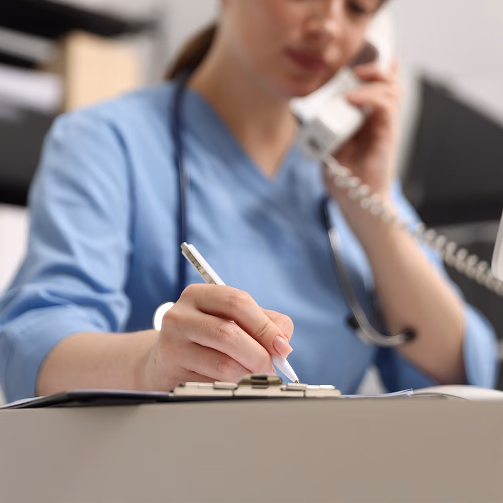 Clinician speaking on the phone while completing patient notes and coordinating care in a medical clinic.